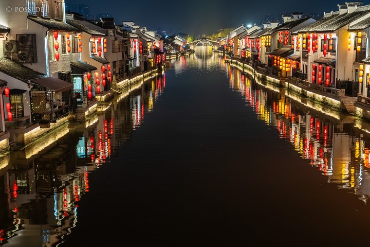 Die Fotografie zeigt eine idyllische Szene mit traditionellen chinesischen Häusern und Laternen an einem Wasserkanal, die eine friedliche Atmosphäre ausstrahlt. (26.03.2025)
