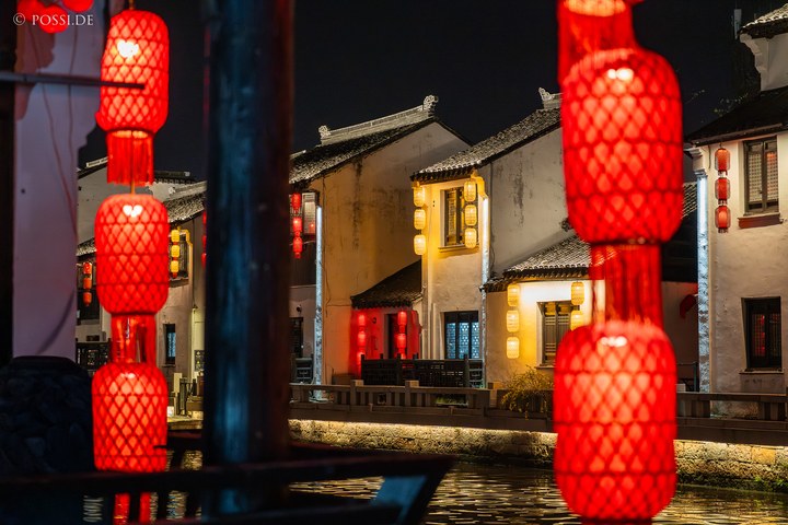 Die Szene zeigt eine idyllische Nachtansicht einer chinesischen Stadt mit traditionellen Gebäuden und roten Laternen. (26.03.2025)