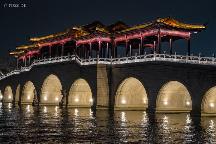 Das Bild zeigt eine Brücke mit einem chinesischen Pavillon, der auf dem Wasser reflektiert wird und eine romantische Atmosphäre erzeugt. (27.03.2025)