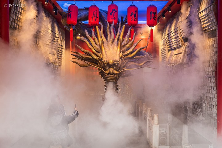 Das Bild zeigt eine Person, die vor einer gigantischen Drachenstatue steht und ein Foto macht. (03.04.2025)