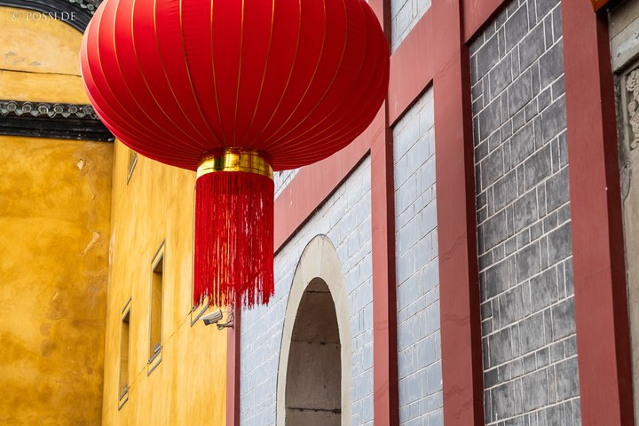 Das Bild zeigt eine rote Laterne vor einer gelben und grauen Wand, die einen asiatischen Stil widerspiegelt. (03.04.2025)